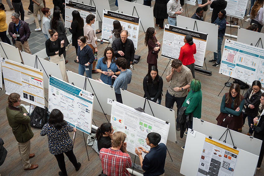 A large group of grad students and faculty looks at the many posters at the Annual Research Day.