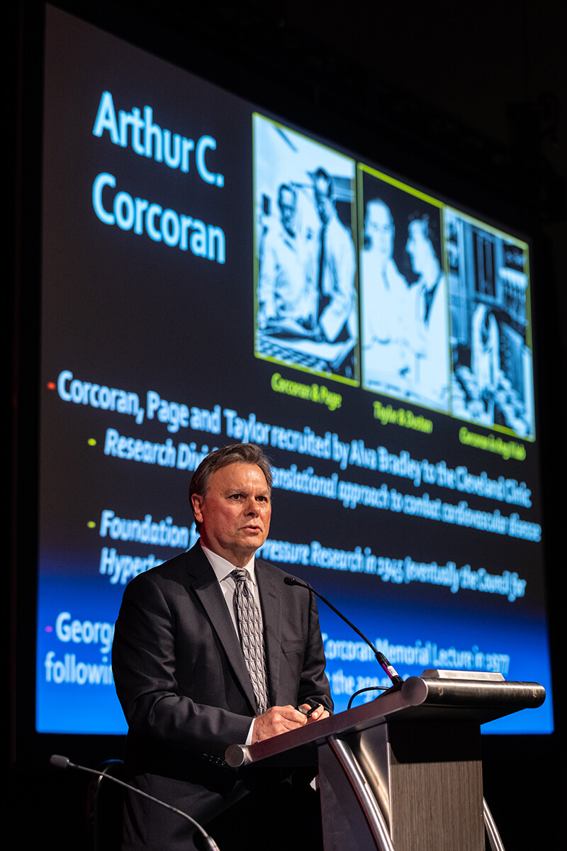 An older man standing behind a podium speaking at a conference.