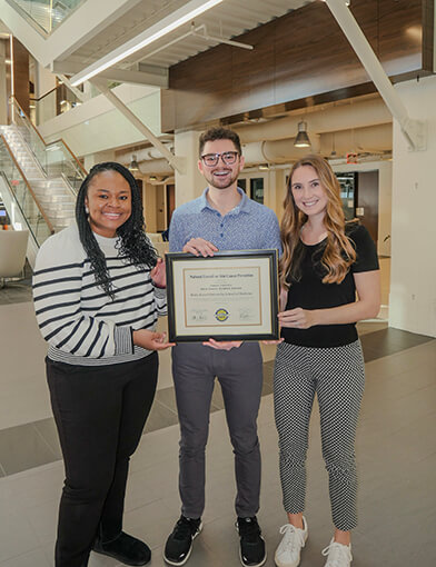 Three students stand and hold a framed certificate.