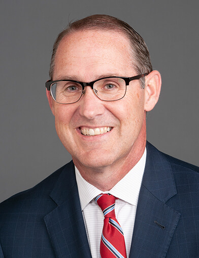 A headshot of a man wearing a red tie and a dark suit jacket.