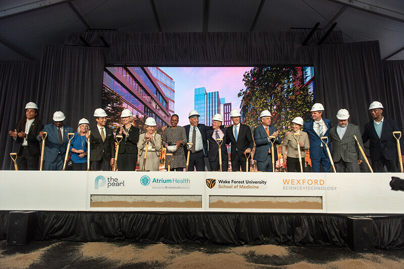 A group of people standing behind a table at a groundbreaking ceremony.