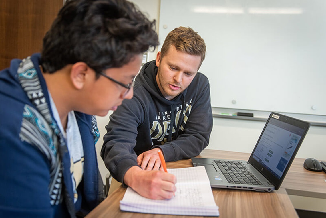 Two people sitting side by side looking at a laptop computer and a notebook. Two people sitting side by side looking at a laptop computer and a notebook.