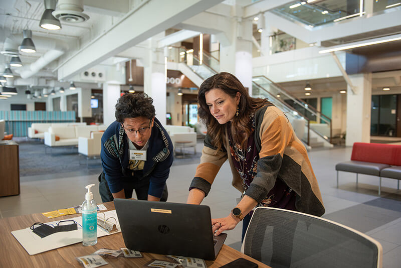 Two people standing and looking at a laptop computer.