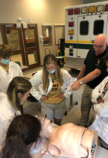 Vertical photo of students in training wearing white coats with yellow Camp Med shirt