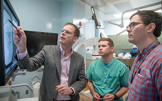 Robert Hurley, MD, PhD, professor of anesthesiology and public health, points to a computer screen and explains something to two male students