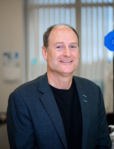 An older man wearing a dark jacket and smiling at the camera.