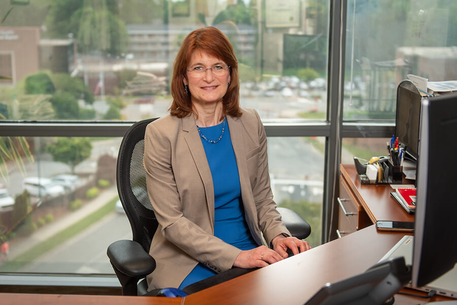 A woman sitting at a desk in front of a large window.