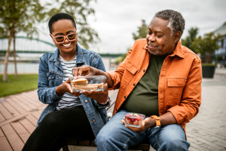 Smiling woman sharing food with man wearing orange jacket.
