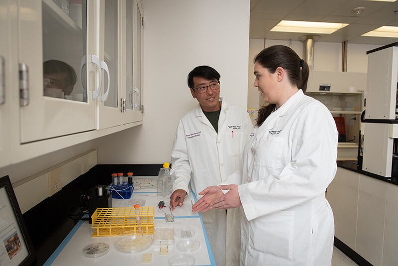 Two people in lab coats having a discussion while looking at medical equipment.