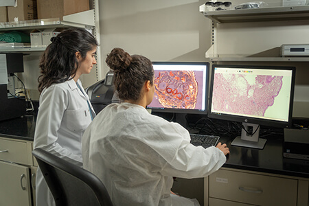 Two women wearing lab coats and looking at medical equipment.