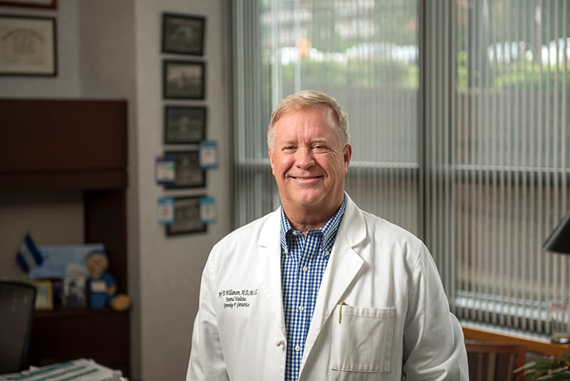 An older man wearing a lab coat smiling at the camera.