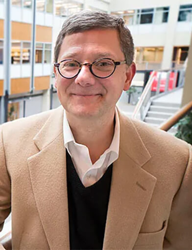A man wearing a tan suit jacket smiling at the camera.