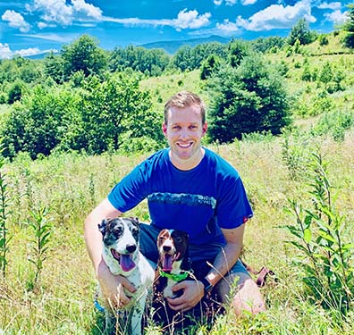 Michael Vollemer with his dogs Abby and Finn in a grassy meadow in the mountains