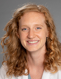 Head shot of young woman with wavy red-gold hair smiling and wearing a white coat