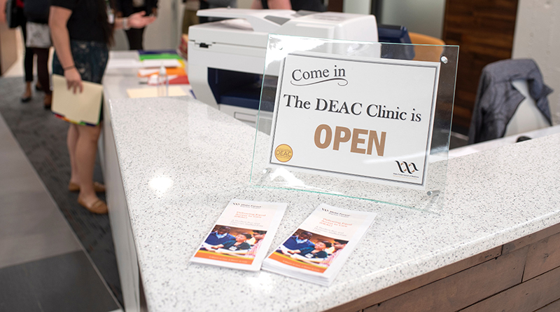 Close-up of sign reading 'The DEAC Clinic is Open' on the corner of a reception counter