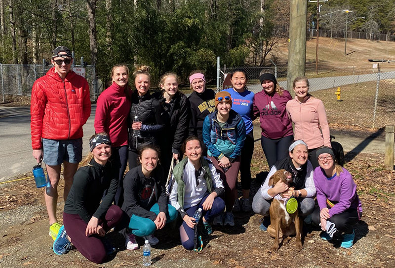 A group of 13 people in cold-weather running gear and one dog pose outdoors