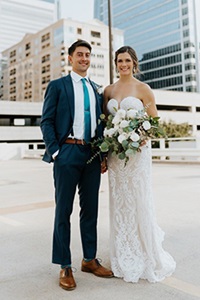 Bride Zoe Hayes and groom Alex Feliciano stand outdoors in an urban setting wearing wedding attire