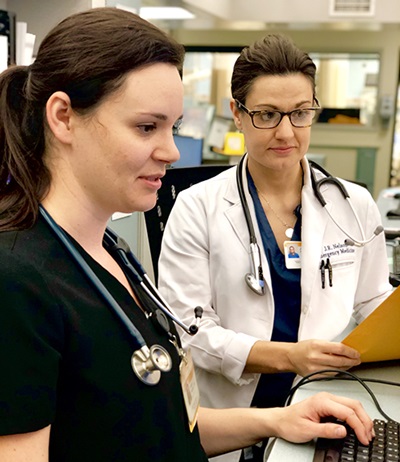 Jennifer Nelson, MD, observes a student wearing black scrubs and entering data into a computer
