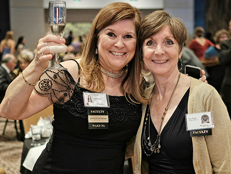 Gail Curtis lifts a glass of champagne in toast to the Wake PA Program's 50th Anniversary as she stands with another woman