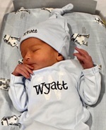 A white newborn wearing a 'Wyatt' onesie and hat sleeps on R2D2 sheets in a bassinet