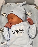 A white newborn wearing a 'Wyatt' onesie and hat sleeps on R2D2 sheets in a bassinet 