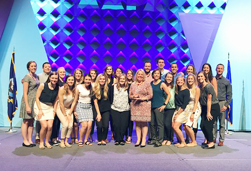 A large group of people stand on a stage with a blue background