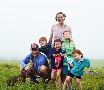 A man, woman, dog and four children laugh as they pose in a green field