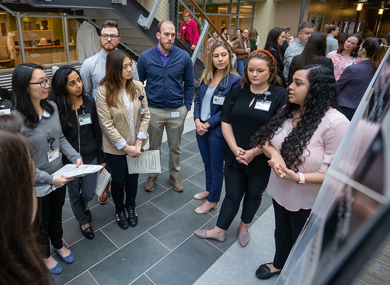 A group of people - mostly women - stand in a circle and listen to one woman who is explaining a poster