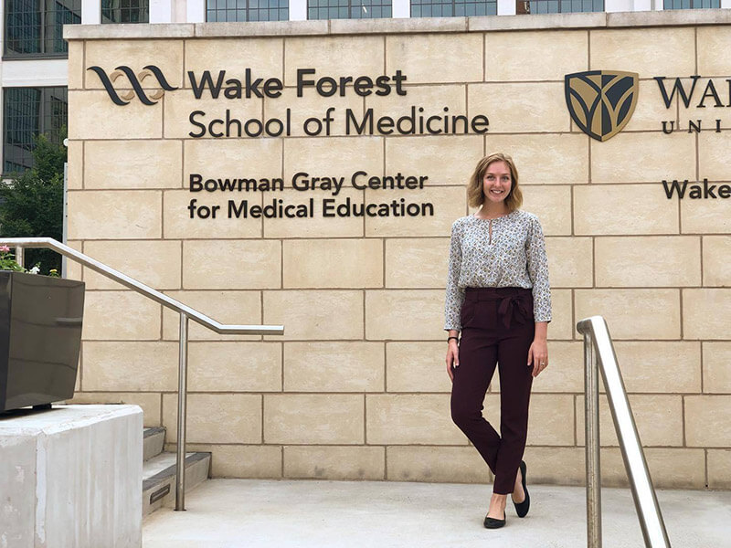A young woman standing in front of a sign that reads Wake Forest School of Medicine Bowman Gray Center for Medical Education.