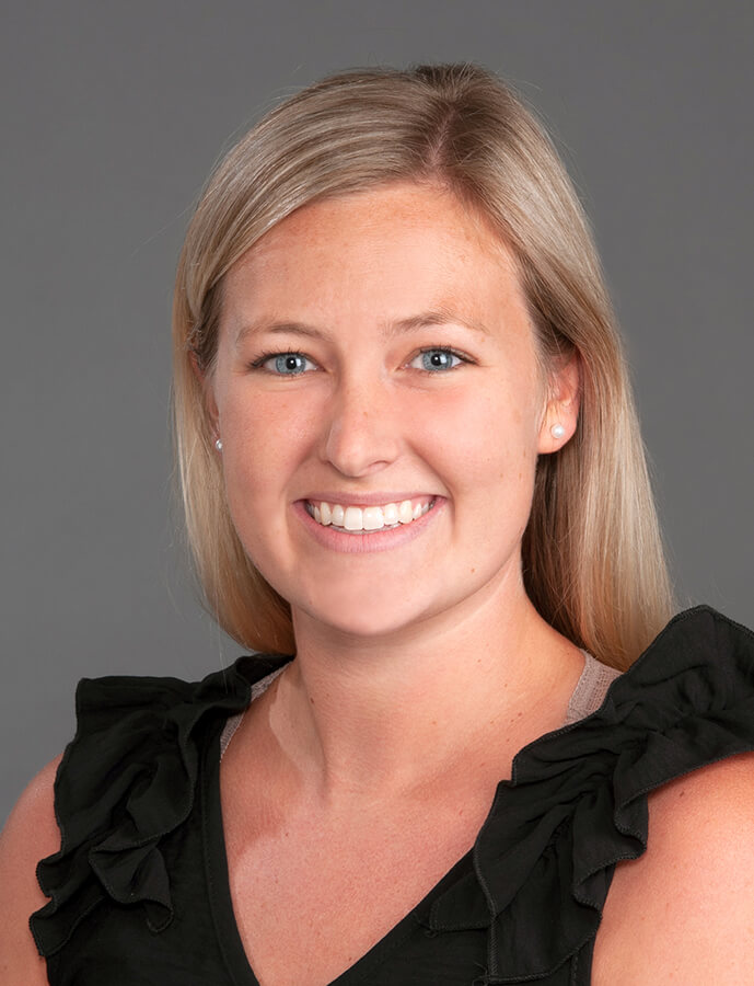 A woman with blonde hair wearing a dark top and smiling at the camera.