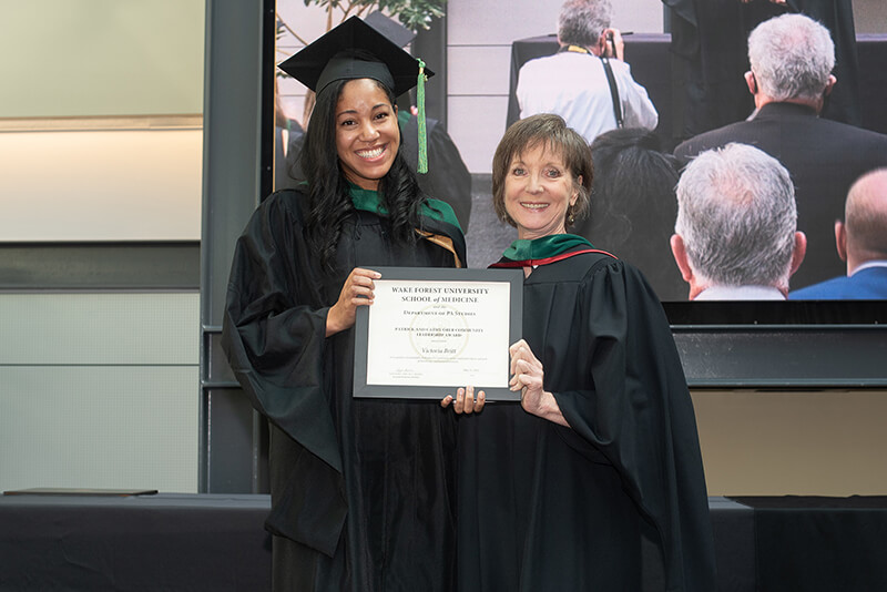 Two women wearing caps and gowns smiling at the camera and holding an award.