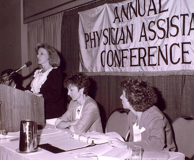 A woman standing at a podium speaking at a conference.