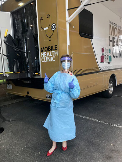 A woman wearing hospital scrubs standing in front of a mobile health clinic.