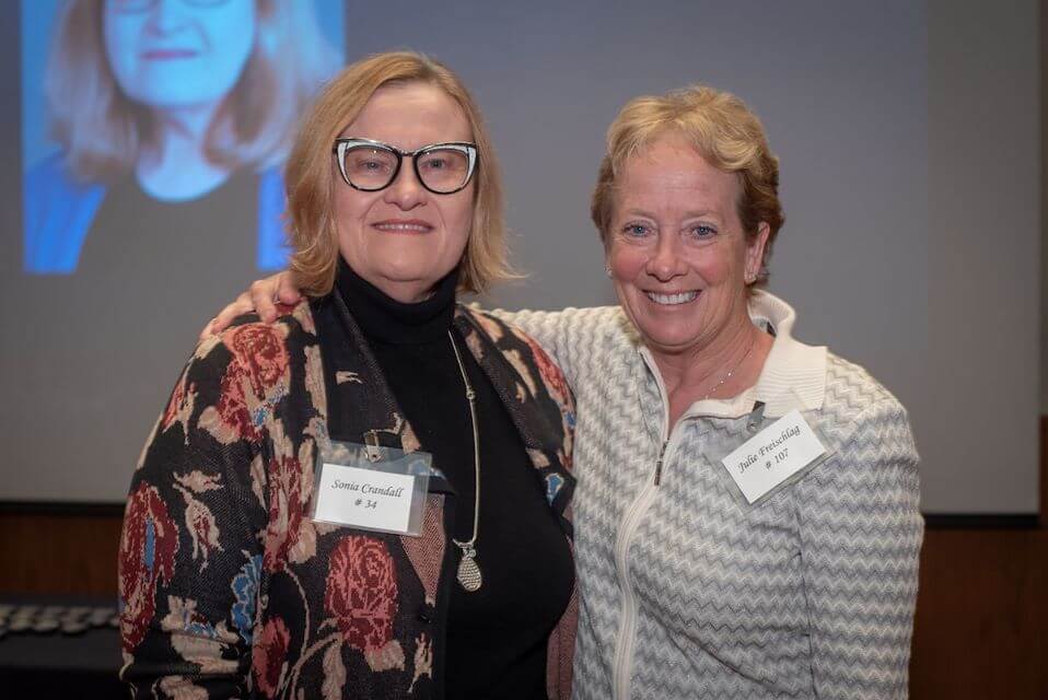 Two women in long sleeve shirts smiling for a photo together.