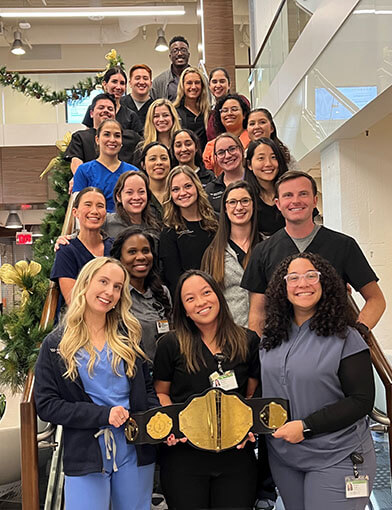 A large group of PA Students in a group on a staircase holding a gold belt.