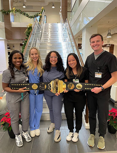 Five PA students, four women and one man, smiling and holding a large gold belt.