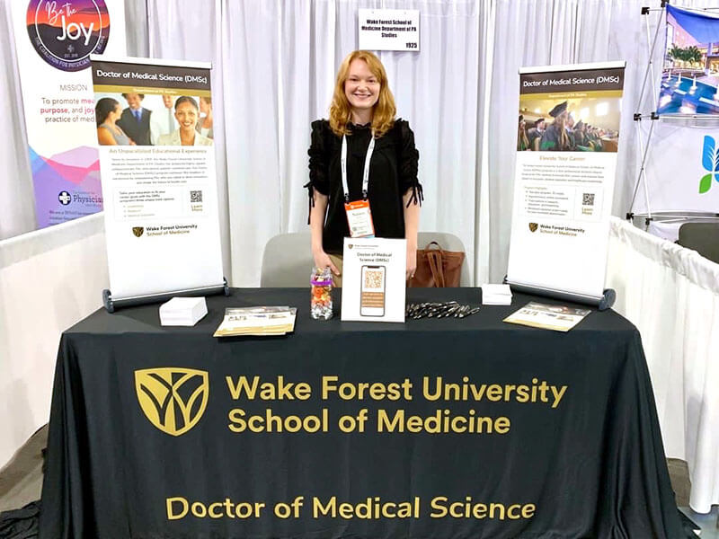 A person standing behind an information booth at at conference.