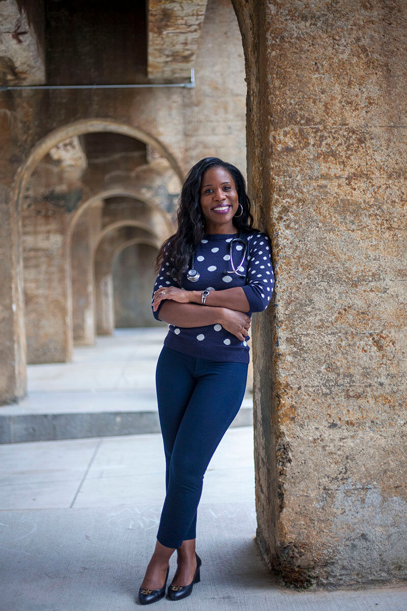 A woman leaning on a column smiling at the camera.