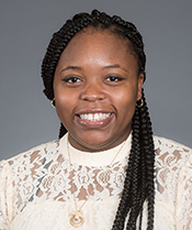 A woman sitting in front of a grey background and smiling at the camera.