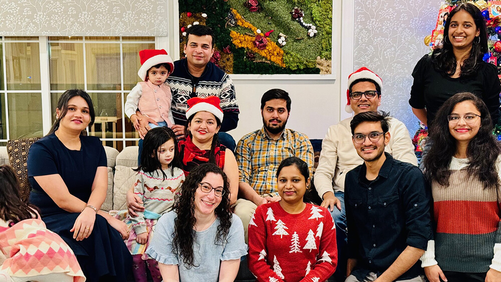 A group of men, women and children in holiday sweaters smile for a group photo in a living room.