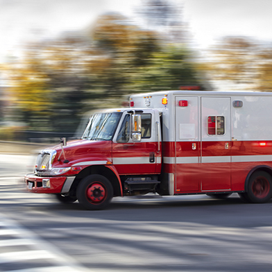 blurred image of red and white ambulance speeding down a street with trees in the background