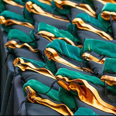 Graduation thumbnail Rows of green and gold stoles lie on a black-clothed table