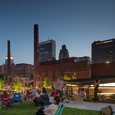 Winston-Salem skyline at dusk in background; people sitting on grass and walking around in foreground