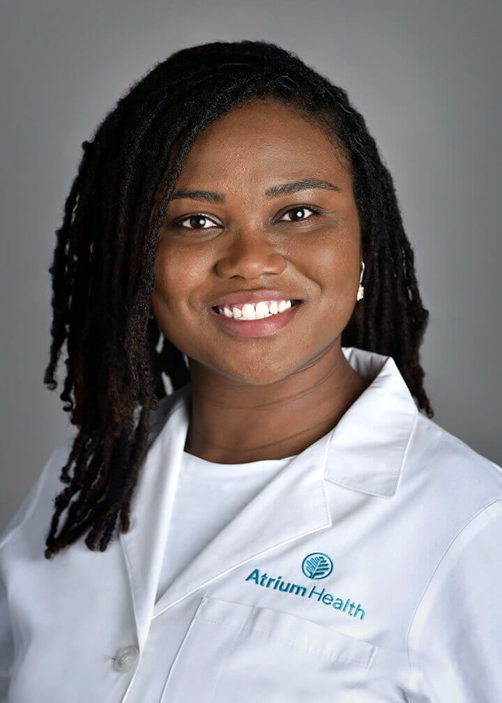 A woman with long hair wearing a lab coat and smiling at the camera.