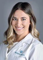 A woman with long blonde hair wearing a lab coat and smiling at the camera.