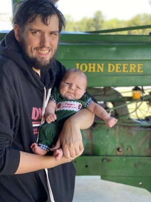 Andy posing with his baby in front of John Deere tractor.