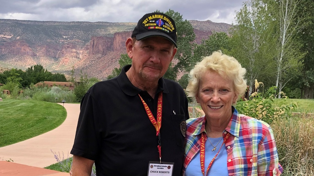 Photo of Kim Roberts on left wearing black shirt, lanyard and baseball camp and Kay Roberts, wearing blue and red plaid shirt overlooking nature.