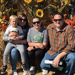 A family of four sitting in front of sunflowers smiling at the camera.