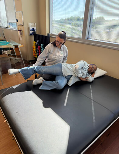 A woman lying down on a raised mat and having a leg held by a medical provider.