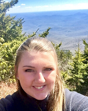 A young woman taking a picture of herself in front of a beautiful mountain view.